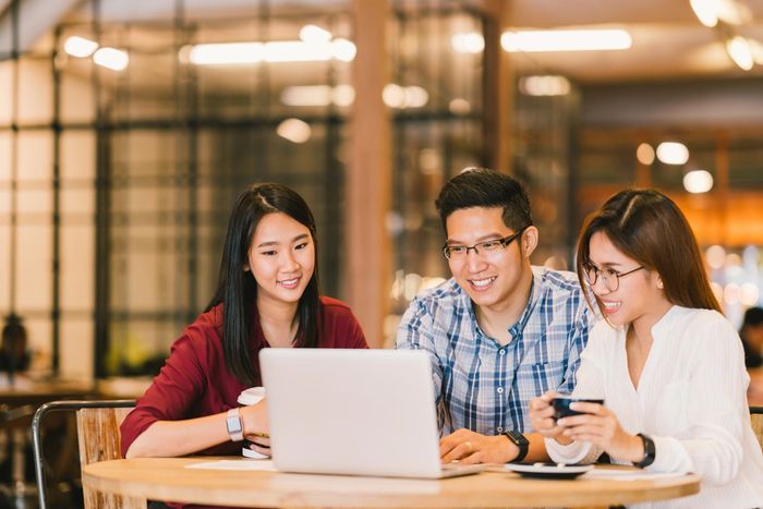 Three people sitting at one table and looking at a laptop