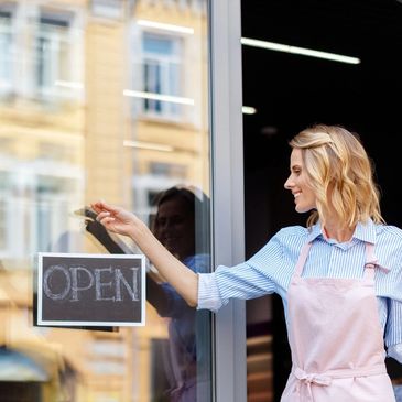 Woman hanging an open sign on a glass door.