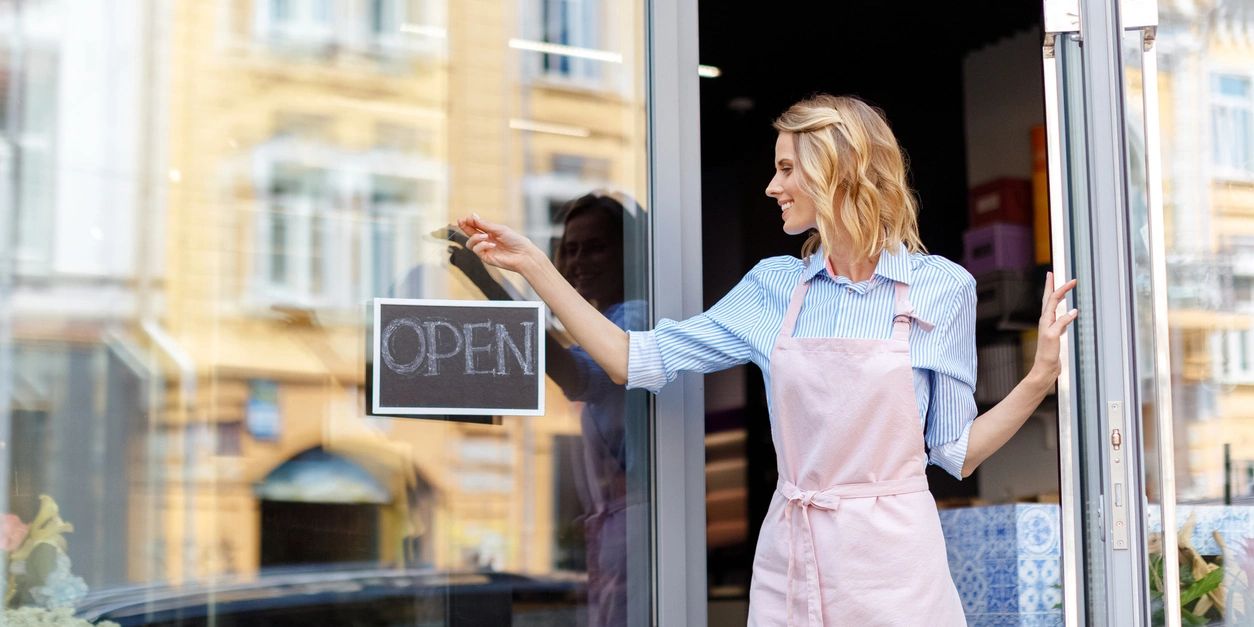 Woman hanging an open sign on a shop door.