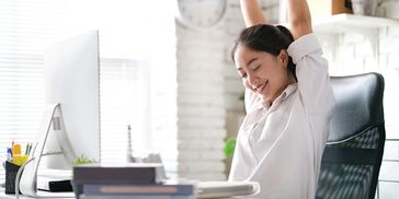 Woman stretching at her desk with a smile in a bright office space.