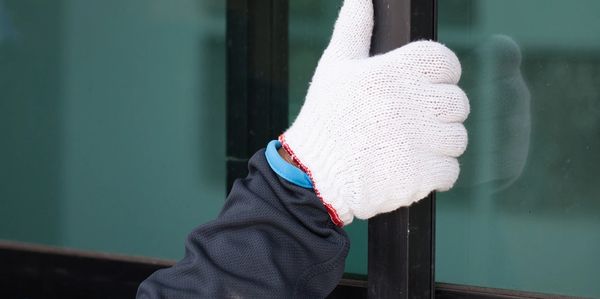 Person wearing a white glove gives a thumbs-up in front of a glass door.