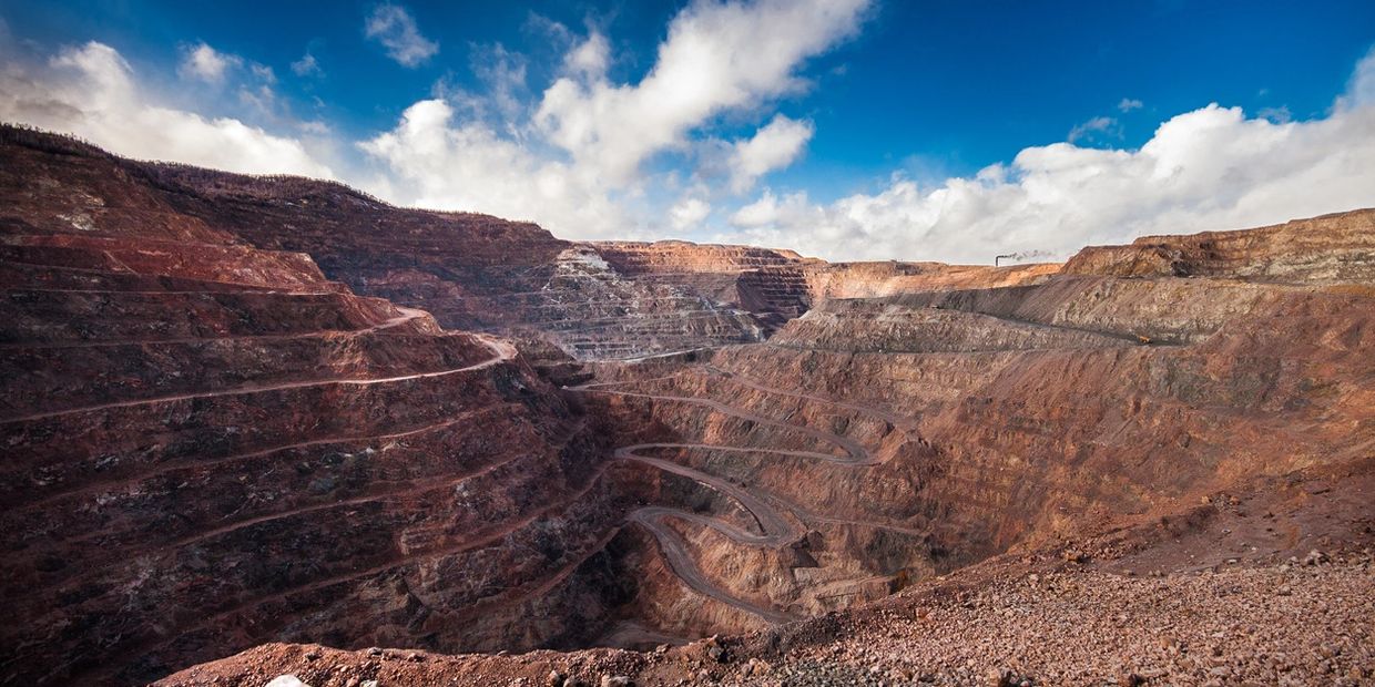 A vast open-pit mine with terraced levels under a partly cloudy sky.