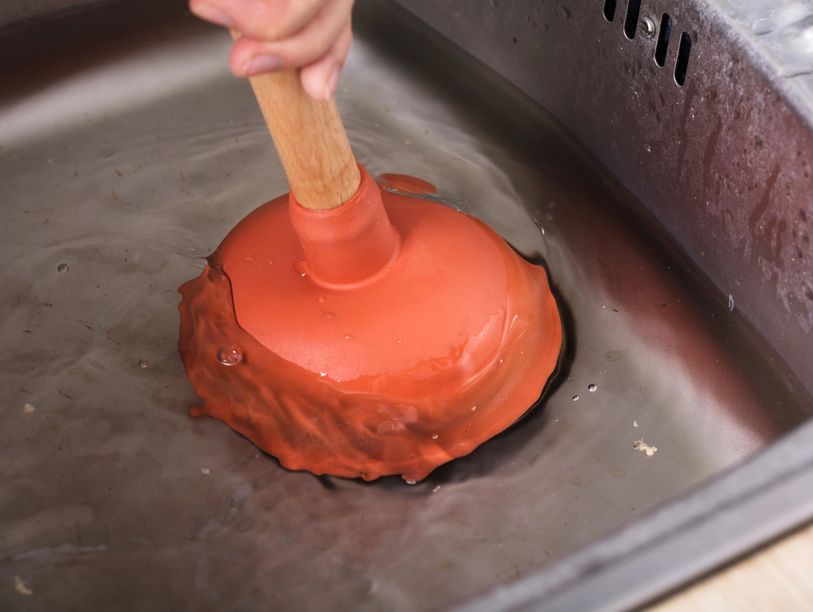 Plunger in a kitchen sink being used to unclog a drain. 