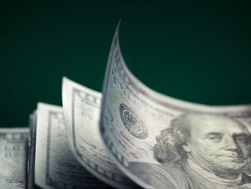 Close-up of U.S. dollar bills fanned out against a dark background.