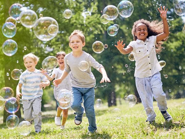 A group of kids chasing bubbles in the grass