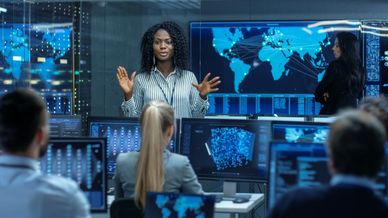 Woman presenting data to a team in a high-tech control room.