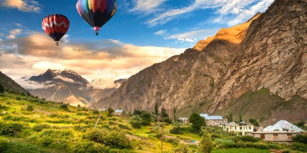 Two colorful hot air balloons float over a mountainous valley with houses.