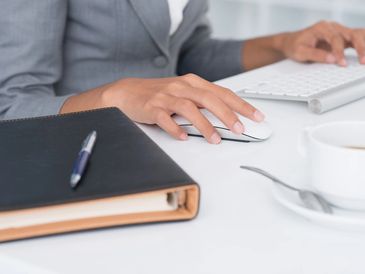 Person using a computer mouse with a keyboard, notebook, and coffee cup nearby.