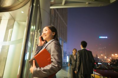 Businesswoman talking on phone outside office building at night.