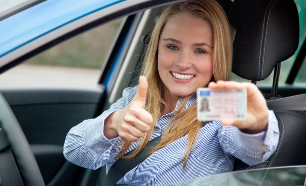 <img alt=" woman holding drivers licence sitting in car">