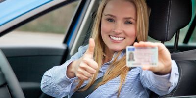 Happy woman in car showing driver's license and thumbs up.