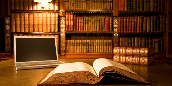 Open book and laptop on wooden desk in a warm library setting.  Happy Reading