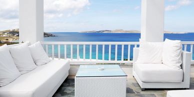 A white balcony with white furniture overlooking the ocean