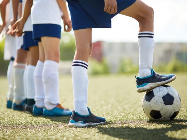 The legs of kids about to do a drill at Football training on turf.