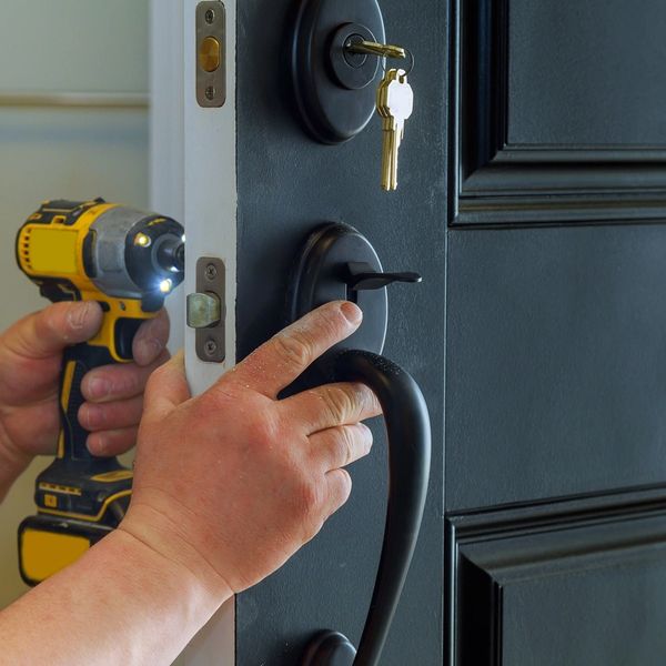 Person installing a black door handle with a cordless drill.