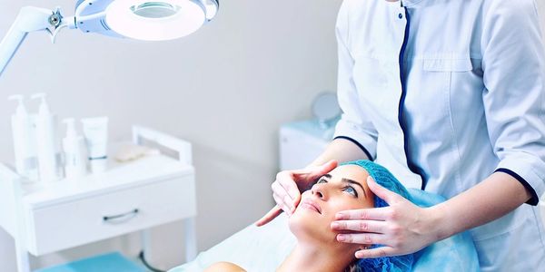 Woman looking down on another woman that is laying on an exam table and looking at her skin.