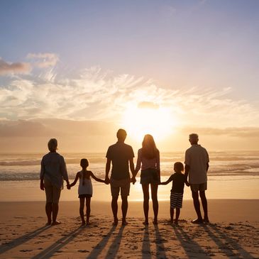 Family holding hands at the beach looking toward the setting sun.