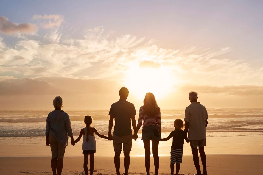 a family of three generations, standing on a beach, looking at the water.