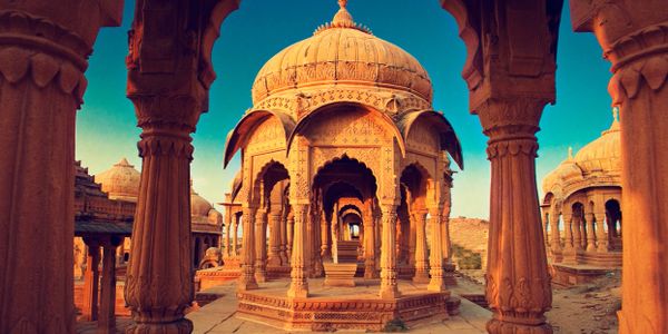 Intricately carved sandstone cenotaphs under a clear blue sky.