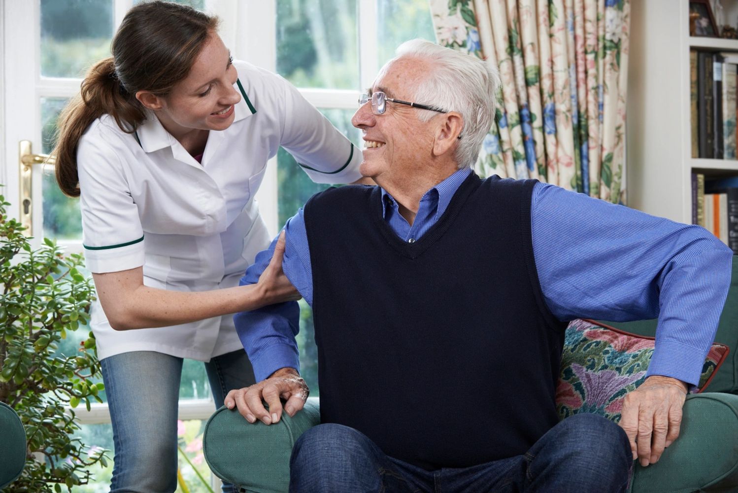 Carer helping an elderly man to get up from the sofa