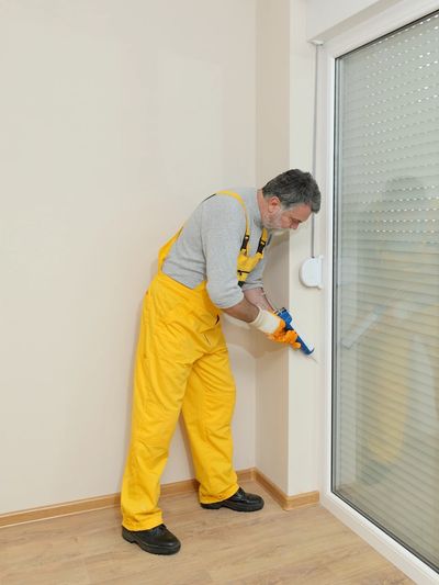 Man in yellow overalls applying sealant to window frame.