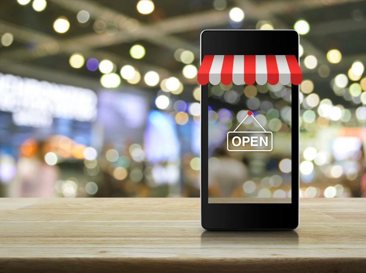 Mobile phone with a digital storefront and open sign on a wooden table.
