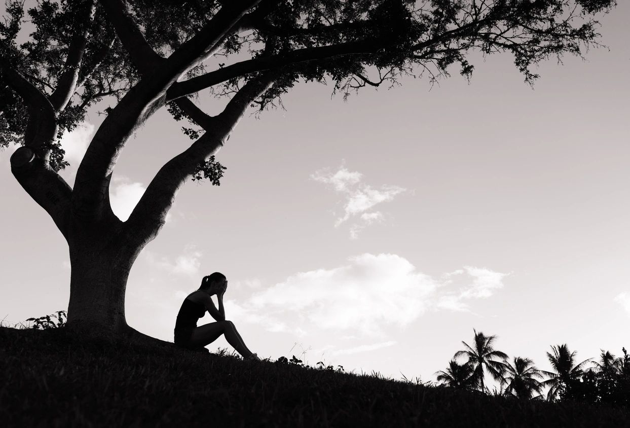Depressed woman sitting under the tree outdoors.