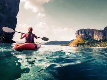 Person kayaking on clear blue water near cliffs.