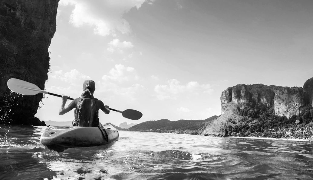 Person kayaking near cliffs and mountains.