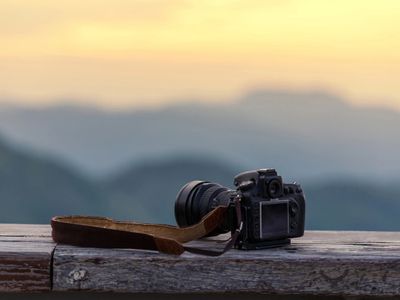 A camera rests on a wooden surface with a blurred mountain backdrop at sunset.