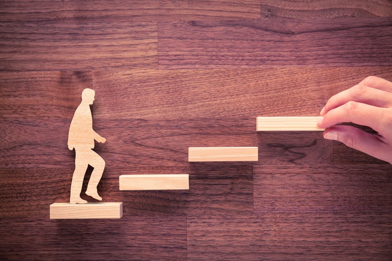 rectangualr wooden steps being placed in front of a wooden cutout of a man, as if assisting in next 