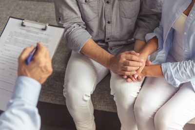 A seated couple is holding hands with therapist nearby