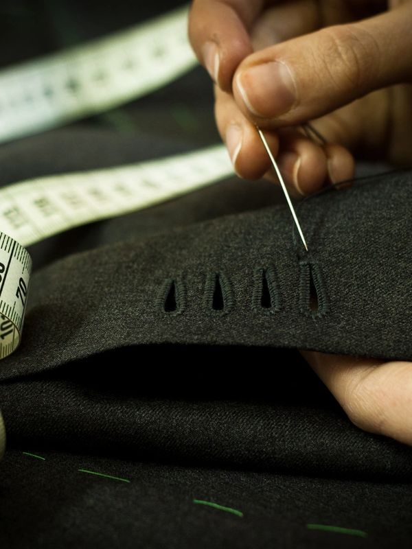 Close-up of hand sewing buttonholes on dark fabric with a measuring tape nearby.
