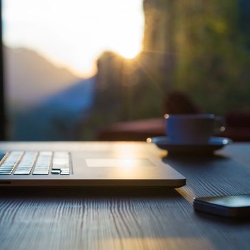 Laptop and coffee cup with sunrise over the mountains in background