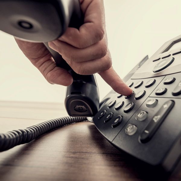 Hand dialing a number on a black office phone.