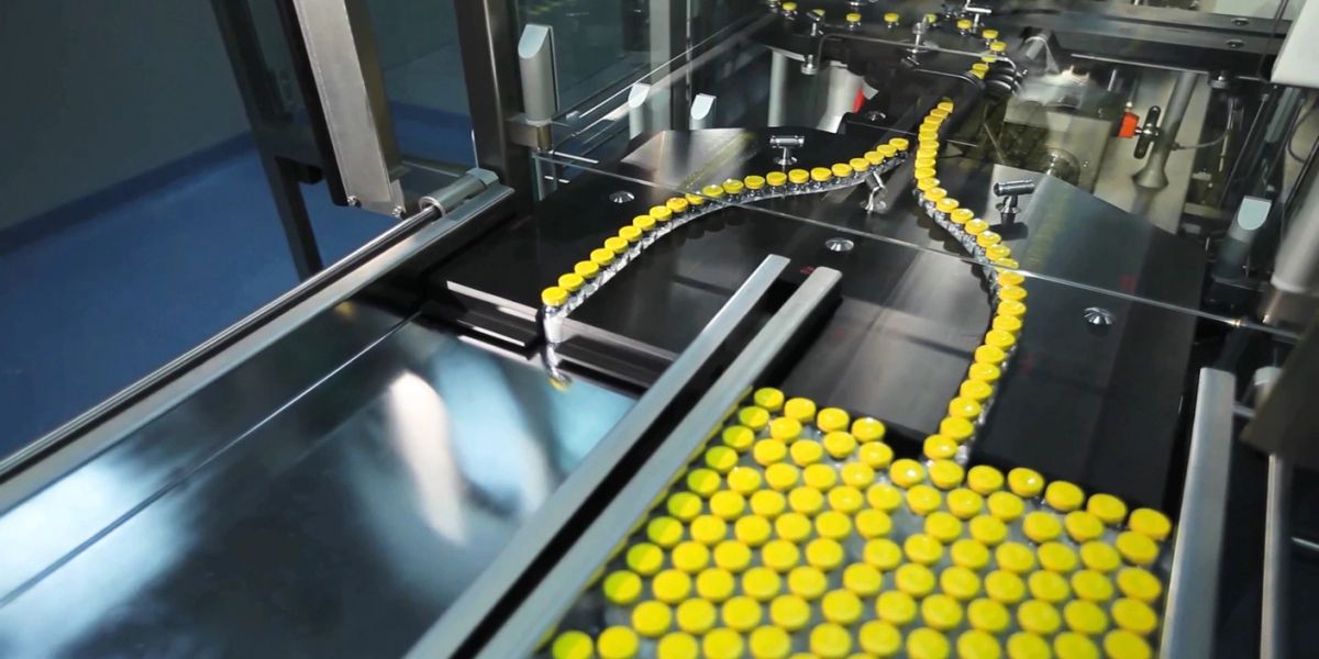 Yellow-capped vials moving along a production line in a pharmaceutical factory.