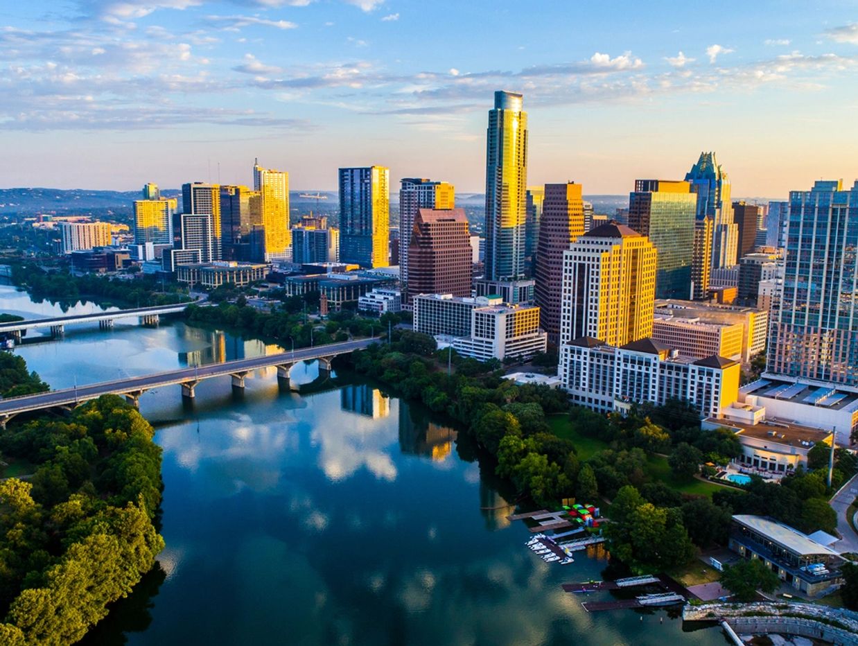Sunlit city skyline with river and bridges at sunset.