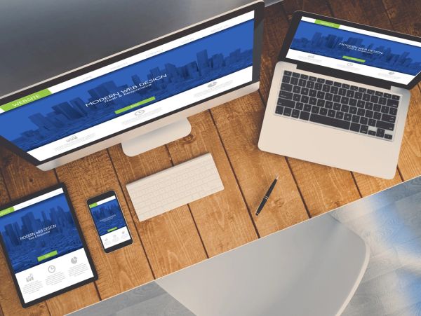 Multiple devices showing responsive modern web design on a wooden desk.
