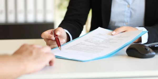 A person in a professional setting handing over an official document in a blue folder to someone.