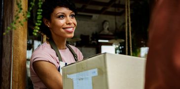 Woman in apron happily handing over a package at a doorway.