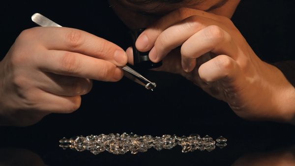 A jeweler inspects a diamond with a loupe and tweezers.