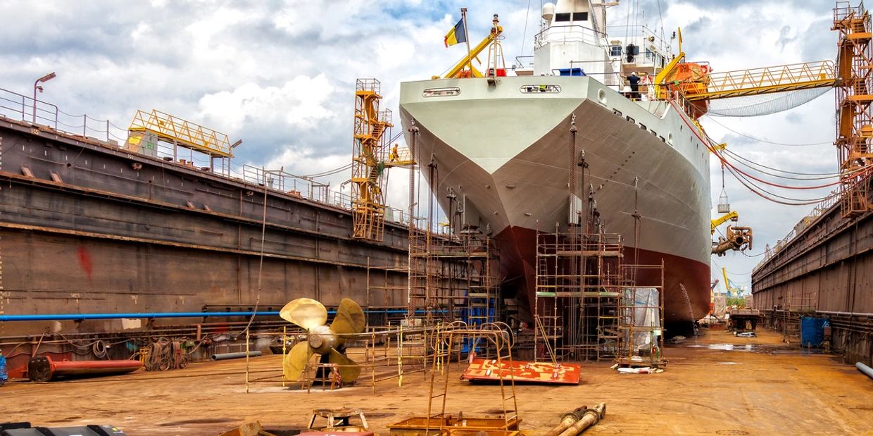 A large ship undergoing maintenance in a dry dock with scaffolding and equipment around it.