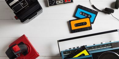Retro gadgets including cassette tapes, game controllers, and a radio on a white surface.