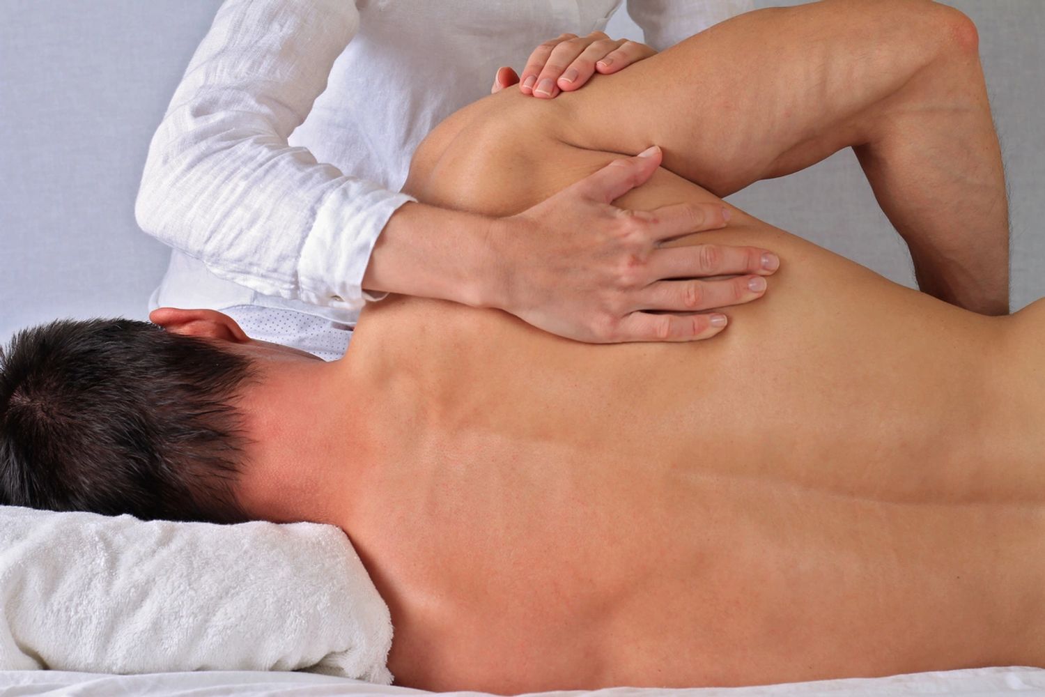 Therapist performing a shoulder stretch on a man's back during a physical therapy session.