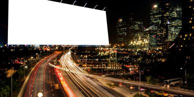 A brightly lit blank billboard overlooks a busy city highway at night.