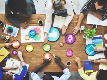 Team collaborating with digital social media icons on a wooden table.