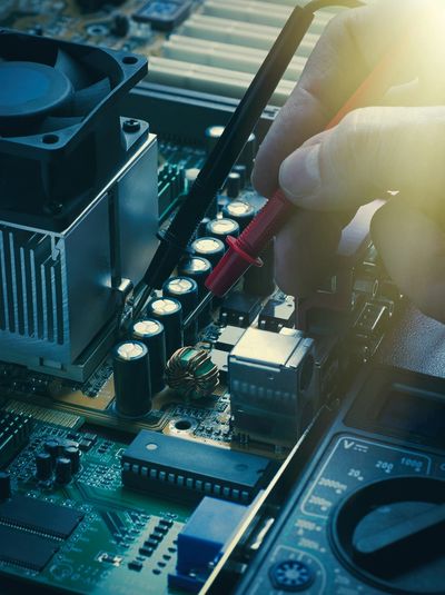 Hand testing computer circuit board with multimeter probes.
