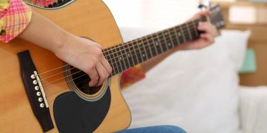 Person playing an acoustic guitar indoors, focusing on the hands and guitar body.