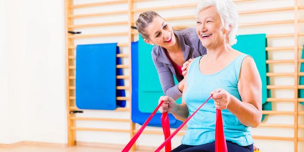 Senior woman exercising with resistance bands guided by a smiling trainer.