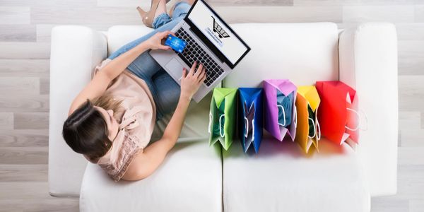 Woman online shopping on her laptop with rainbow shopping bags next to her.